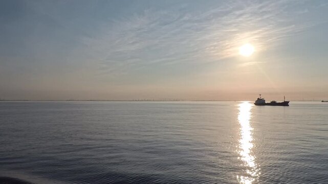 Cinematic video of a cargo ship silhouette near a brilliant sunroad on the ocean at sunrise