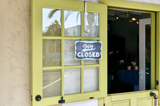 Sorry Closed sign hanging on a light green wooden door of a cafe, store or boutique shop. Small local business window display, retail storefront exterior backdrop and working hours concept.