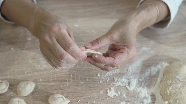 Traditional food preparation process showing hands making handmade dumplings with meat filling from dough on a floured kitchen surface