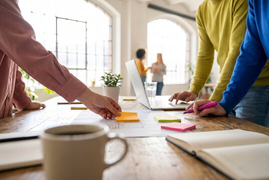 Close up of hands arranging sticky notes on blueprint during creative team meeting