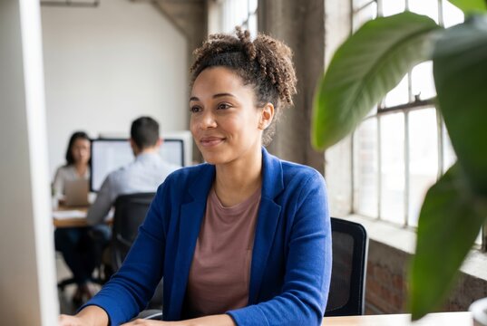 Confident young businesswoman smiling at desk in bright plant filled creative office