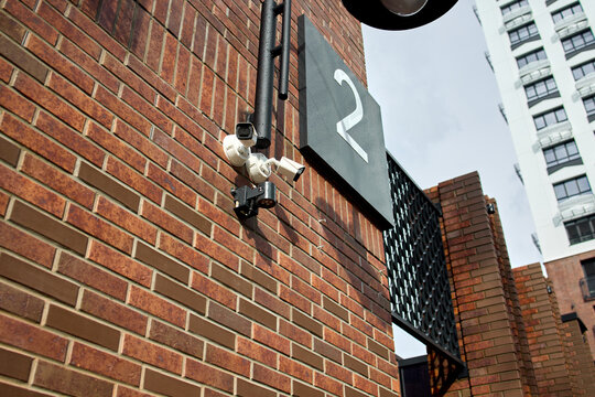 Security camera installed on brick wall, in urban building exterior, with brick wall, security camera, number 2 sign, from a close-up perspective perspective, with brown, gray accents.