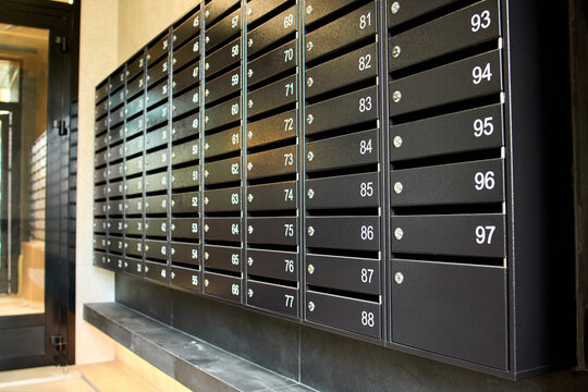 metal mailboxes on a concrete building facade in a neutral side view of real estate commercial properties with black and gray tones and natural light, clean background.