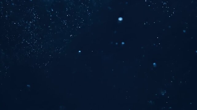 Abstract dark blue background with blurry sparkles and ethereal dust motes