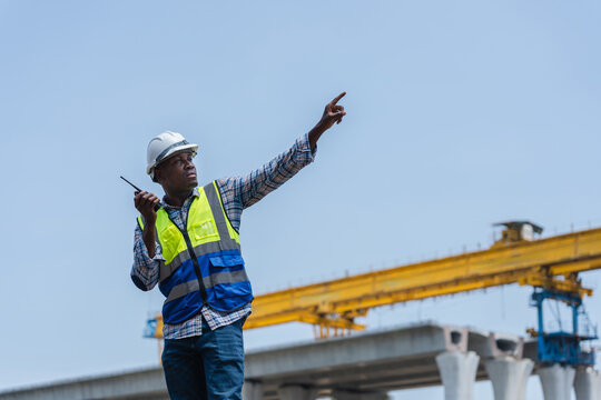 Construction foreman using walkie-talkie and pointing at construction site, Engineer monitoring infrastructure project with radio communication, Supervisor directing operations at building site