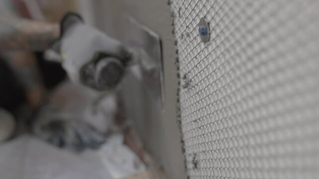 This video shows a close up of a tattooed construction worker's arm applying mortar to a metal lathe on a wall.