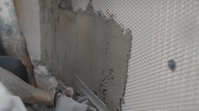 This video shows a construction worker carefully applying mortar to a metal lathe on a wall with a trowel.