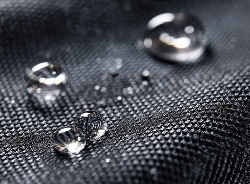 Close-up showcases droplets resting on a dark, textured fabric. Focus highlights surface tension and the fabric's pattern