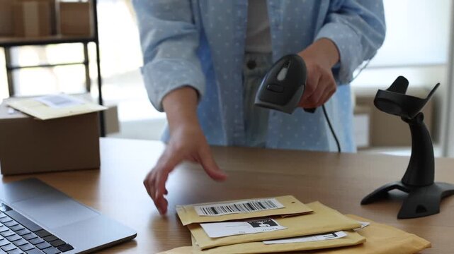 Post office worker with scanner reading barcode on envelopes at desk indoors, closeup