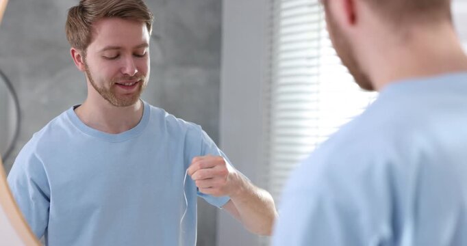 Man using dental floss near mirror indoors. Oral hygiene