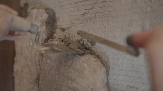 This video shows a close up of a specialty tool filling mortar gaps around a rock just placed by a mason on a rock wall.