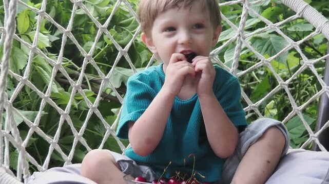 Cherry in kids mouth. Cherry fot kids. Happy kid eating ripe, sweet, juicy, fresh cherries. Child holding cherries. Concept of healthy summer food.
