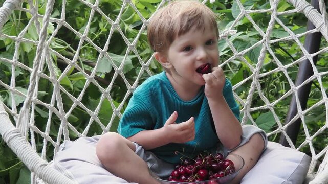 Cherry in kids mouth. Cherry fot kids. Happy kid eating ripe, sweet, juicy, fresh cherries. Child holding cherries. Concept of healthy summer food.