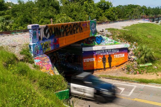Graffiti-covered underpass bridge with memorial mural and passing car