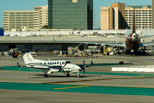 LAX, Los Angeles, California, USA - January 7, 2026 - Beechcraft King Air turboprop taxiing on the tarmac at LAX with a Virgin Airlines Jumbo aircraft at the terminal and Sheraton and Sonesta hotels