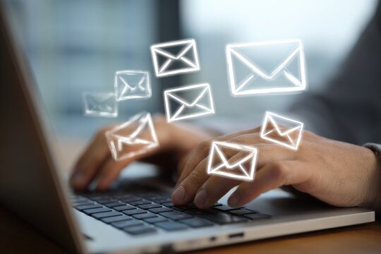 Close-up of hands typing on a laptop, with ethereal glowing email envelope icons floating above. Focus on technology