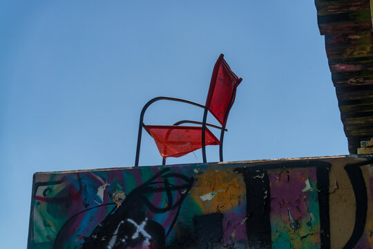 Red chair on graffiti-covered rooftop against blue sky