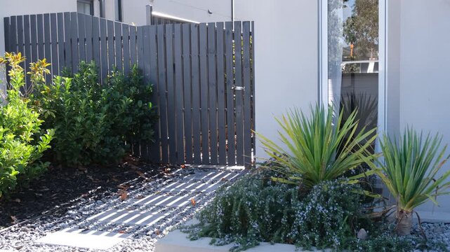 A timber gate opens beside drought-tolerant landscaping at a modern home's side entrance. Low-maintenance garden design in a new-build suburban homes in Australia.