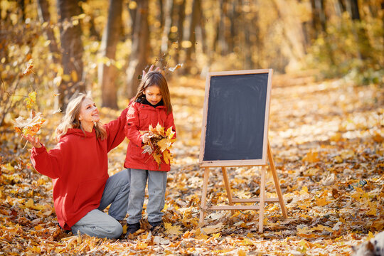 Mother and daughter playing in autumn forest near easel