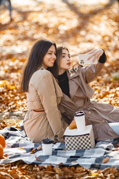 Two girls have picnic on a blanket in autumn park and make a selfie