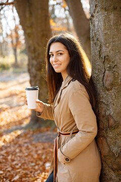 Young woman standing near tree and holding a cup of coffee