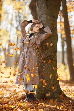 Young woman standing near tree and posing for a photo in autumn park