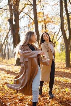 Two girls friends walking together in autumn park