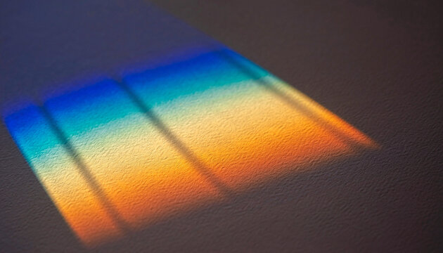 Sunlight passing through a prism creates a spectrum of colors on a surface, producing a rainbow-like pattern with vibrant hues and shadow effects.