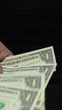 A detailed closeup of a person counting several US one dollar bills against a dark minimalist background. Useful for financial, poverty, or small business concepts.