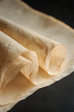 Rolled parchment paper with light brown staining and creased edges is presented on a dark surface. AI.