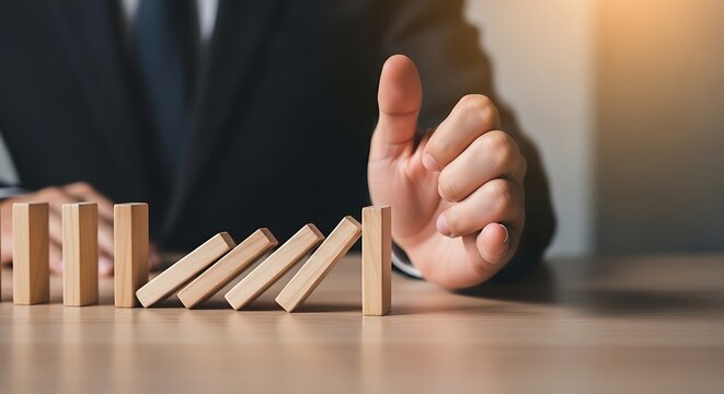 Businessman stopping falling wooden dominoes concept of risk management