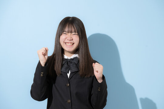 水色背景で制服で立つカメラ目線笑顔の女子中学生や高校生のイメージ　ガッツポーズで元気