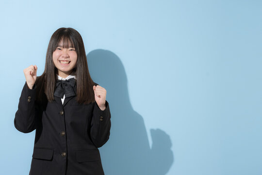 水色背景で制服で立つカメラ目線笑顔の女子中学生や高校生のイメージ　ガッツポーズで元気