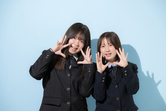 水色背景で制服で立つカメラ目線笑顔の女子中学生や高校生のイメージ　応援や声援の口コミ、レビューのポーズ