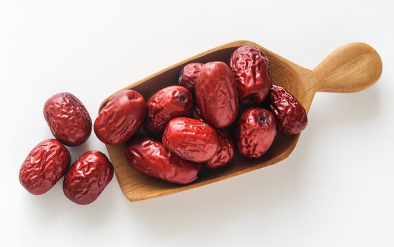 A wooden scoop filled with dried jujubes (Chinese red dates), highlighting their wrinkled texture and rich reddish color.