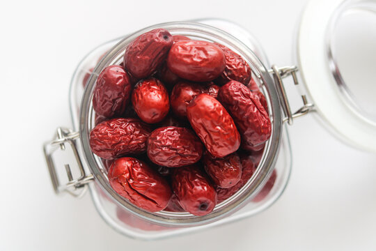 Top-down view of a transparent glass jar filled with dried jujubes (Chinese red dates), showcasing their rich reddish color and natural texture.