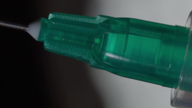 Macro closeup panning across a medical syringe showing the needle, transparent barrel, and dosage measurement markings with shallow depth of field in a clinical setting