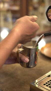 Barista hand steaming milk with espresso machine steam wand in cafe