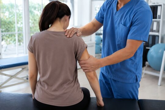 Physical therapist in blue scrubs examining female patient shoulder joint