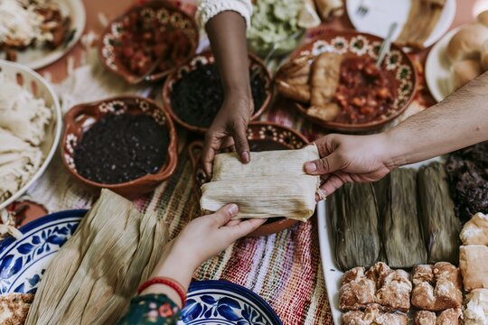 Hands passing a steaming tamale across a crowded table filled with traditional Latin American food for a festive family gathering and community dinner