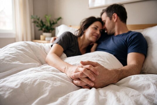 Happy couple lying in bed together, holding hands and looking at each other with love and affection