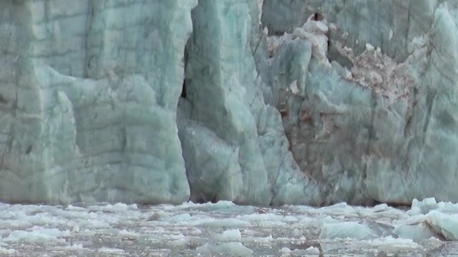 The magnificent face of an Arctic glacier dominates, its deep blue hues hinting at immense age. Below, countless fragments of ice drift gently upon the cold ocean surface under a bright sky.