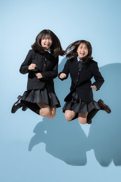 水色背景でジャンプする躍動感のある日本人女子高生や中学生　2人で前向きに進む成長や受験や青春、嬉しいや楽しいハッピーなイメージの全身の正面