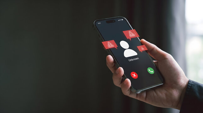Spam call and phishing concept: Hand holding smartphone with unknown caller and red warning alert icons, Cyber security and scam alert, Hand holding mobile phone with suspicious unknown caller.