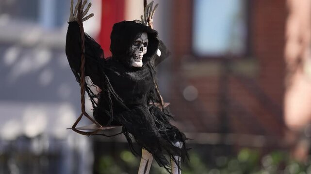 Halloween Grim Reaper Skeleton Decoration on Swing Outdoors. Creepy Halloween skeleton decoration sitting on a swing outdoors. Spooky seasonal display with skull, black hooded robe, and eerie autumn