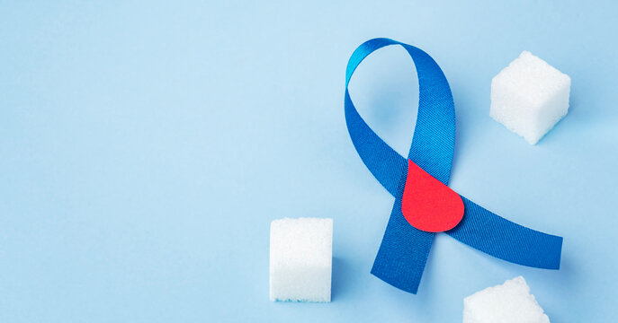 Blue ribbon and red blood drop with sugar cube on blue background, world diabete day concept
