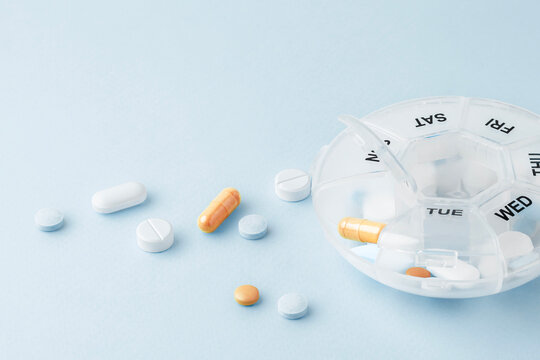 Pill box with pills and supplements on light green blue background
