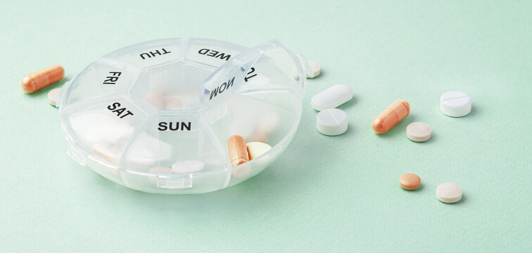 Pill box with pills and supplements on light green background