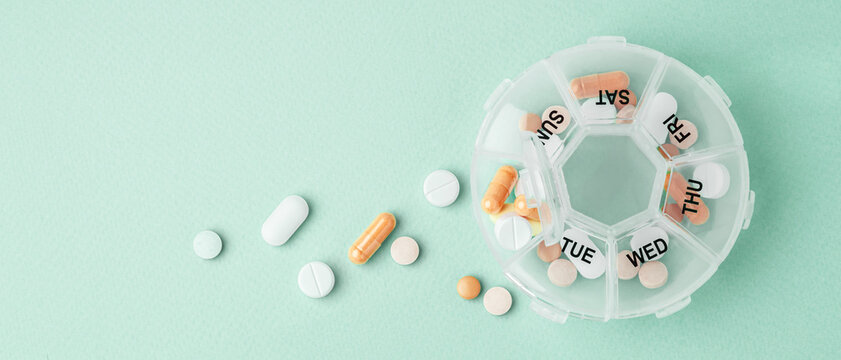 Vitamins and supplements with daily pill box on light green background, top view