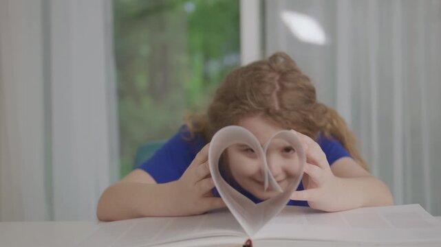 Love reading book concept. Child Creating Heart Shape with Book Pages. Kid forms a heart shape with book pages while reading at home. Love of books, education, childhood learning, literacy.